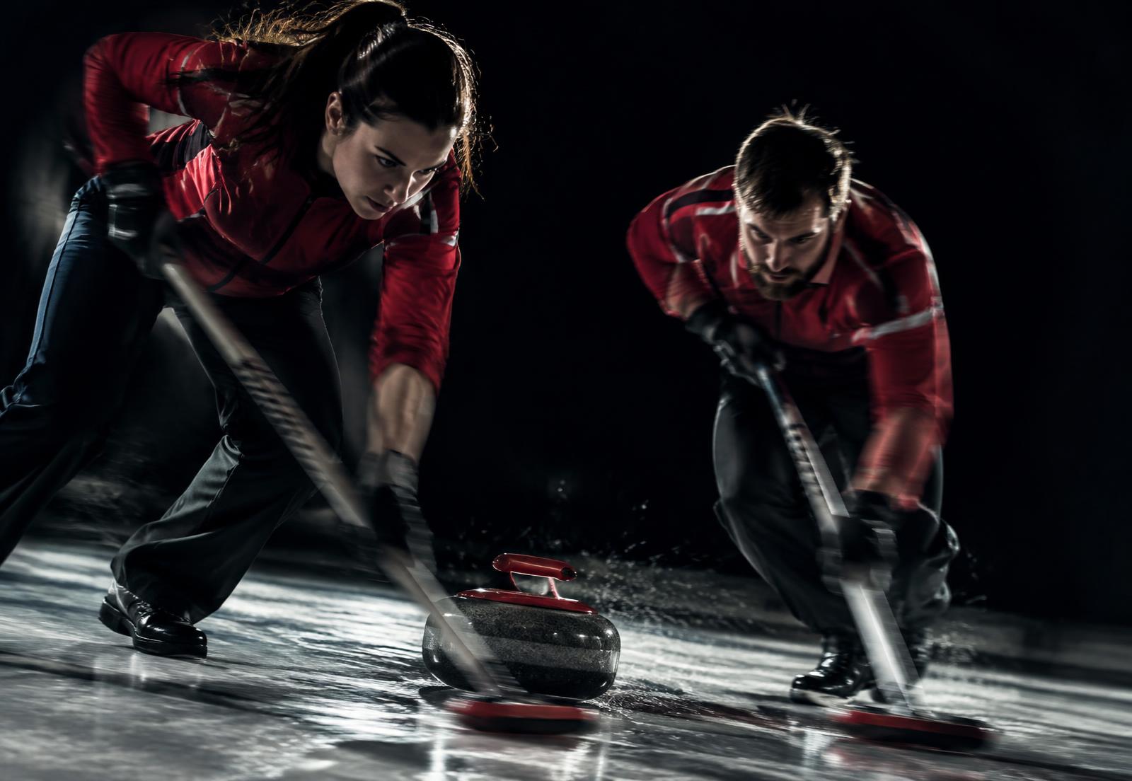 Dva igralca curlinga z metlama drgneta led pred kamnom